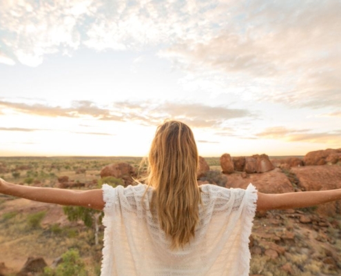 Frau mit ausgebreiteten Armen steht bei Sonnenaufgang in weiter Landschaft – Karfreitag spirituell als Bild von Hingabe und Auferstehung