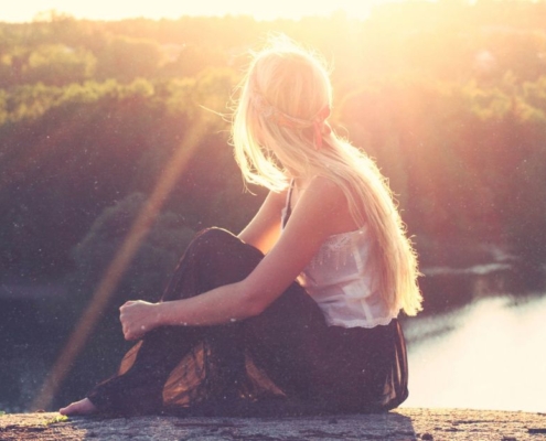 Frau sitzt barfuß am See im Sonnenuntergang, Sinnbild für Frauen in der Bibel und ihre zeitlose Kraft