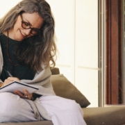 rauhnaechte-wuensche-erfuellen-sich-nicht-journaling Frau sitzt lächelnd journaling auf dem Sofa und schreibt in ihr Notizbuch. Rauhnächte-Wünsche erfüllen sich nicht sofort, sie entfalten sich über das ganze Jahr